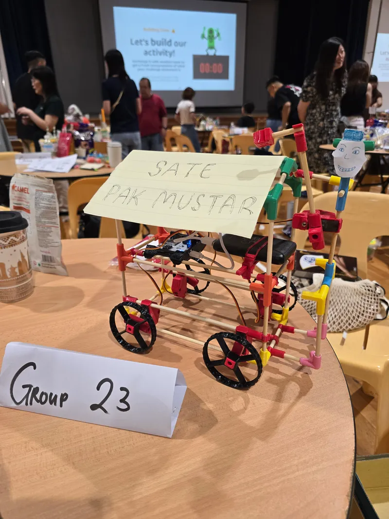 A robot built as a satay cart with a hand-written sign, on a group’s table
