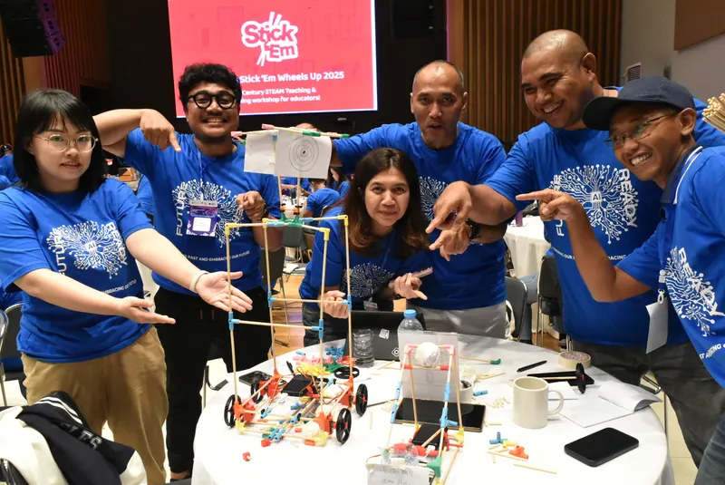 Teachers in matching shirts pointing at the tall build on their table