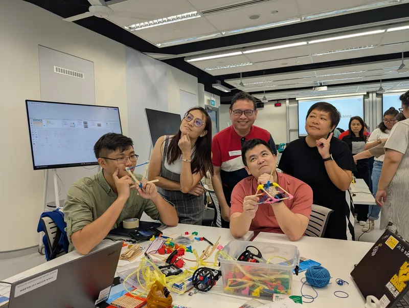Five teachers at a makerspace table, one holding up a small triangular build